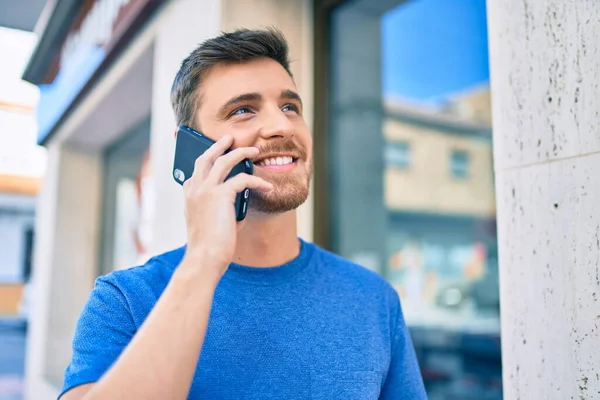 Genç beyaz adam gülümsüyor. Şehirdeki akıllı telefondan konuşuyor..