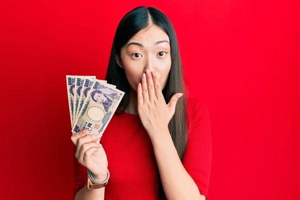 Młoda Chinka Trzymająca Japońskie Banknoty Jenowe Zakrywające Usta Ręką Zszokowana — Zdjęcie stockowe