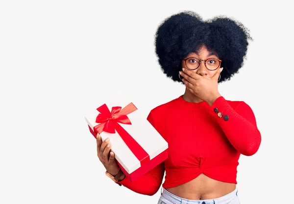 Chica Afroamericana Joven Sosteniendo Regalo Impactado Cubriendo Boca Con Las — Foto de Stock