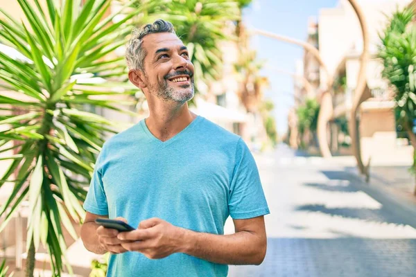 Středního Věku Šedovlasý Muž Úsměvem Šťastný Pomocí Smartphone Chůze Ulici — Stock fotografie