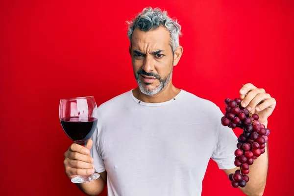 中世の白髪の男は 新鮮なブドウと赤ワインの無色混乱した表現の枝を保持します 疑わしい概念 — ストック写真