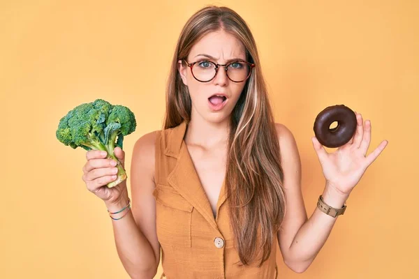 Giovane Ragazza Bionda Con Broccoli Ciambella Cioccolato Faccia Shock Dall — Foto Stock