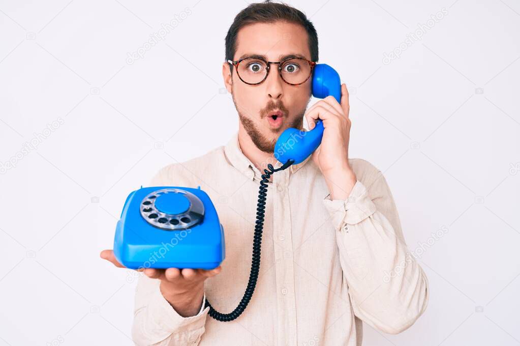 Young handsome man holding vintage telephone scared and amazed with open mouth for surprise, disbelief face 