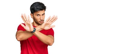 Kırmızı tişört giyen yakışıklı bir genç. Reddedilmiş yüz ifadesi. Kollar çapraz, avuç içleri negatif, kızgın yüz ifadesi. 