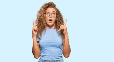 Gündelik giysiler ve gözlük takan güzel beyaz kız hayret ve şaşkınlık içinde başını kaldırıp parmaklarıyla işaret etti ve kollarını kaldırdı.. 