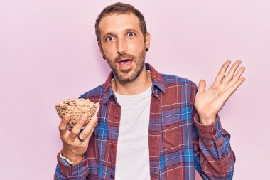 Genç yakışıklı adam elinde mısır gevreği tutarak başarıyı mutlu bir gülümsemeyle ve kazanan yüz ifadesiyle kutluyor. 