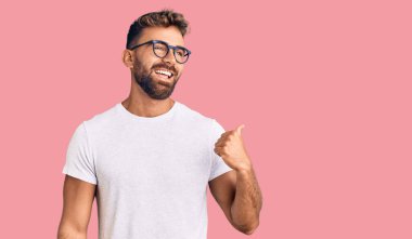 Gündelik kıyafetler ve gözlük takan, gülen yüzlü gülümseyen ve başparmağıyla yan tarafı gösteren İspanyol genç adam.. 