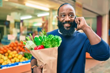 Elinde süpermarketten alınmış kağıt torba sakallı Afrikalı Amerikalı adam telefonda konuşuyor.