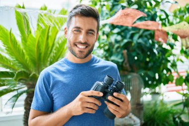 Parkta dürbünle gülümseyen yakışıklı bir genç.