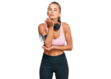 Spor kıyafetleri giyen ve kulaklık takan genç sarışın kadın havayla öpüşürken kameraya bakıyor. Güzel ve seksi. aşk ifadesi. 