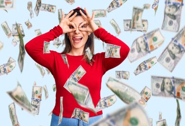 Genç ve güzel bir kadın günlük kıyafetler giyip dürbün gibi jest yapıyor, gözleri parmaklarından bakıyor. çılgın ifade.