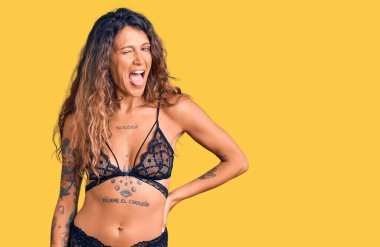 Dövmeli, iç çamaşırlı, seksi bir ifadeyle kameraya bakan, neşeli ve mutlu yüzlü genç bir İspanyol kadın.. 