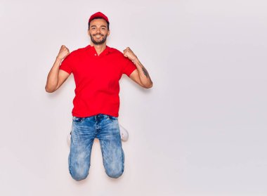 Mutlu gülümseyen üniformalı yakışıklı İspanyol teslimatçı. Yüzünde tebessümle zıplıyor, beyaz arka planda yumruklar havada kutluyor..