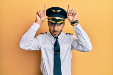 Yakışıklı İspanyol pilot üniforması giymiş komik jestler yapıyor ve parmağıyla boynuzlarını çıkartıyor. 