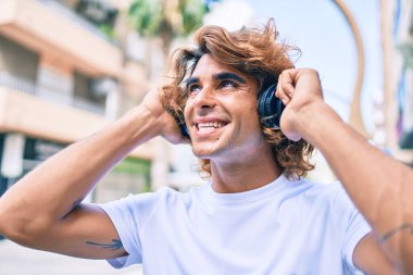 Genç, yakışıklı, gülümseyen, kulaklık takan, şehir sokaklarında yürüyen bir İspanyol.