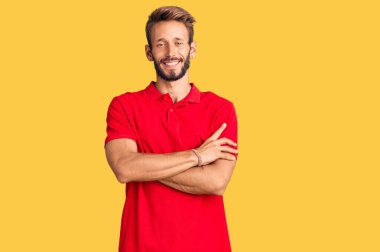 Sarışın, sakallı, sıradan giyinen mutlu yüzlü, kollarını kavuşturup kameraya bakan yakışıklı bir adam. pozitif kişi. 