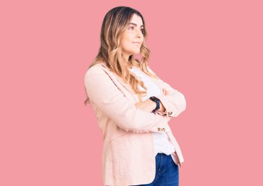 İş kıyafetleri giymiş genç beyaz bir kadın kollarını kavuşturmuş ve kendinden emin bir şekilde yan tarafa bakıyor. 