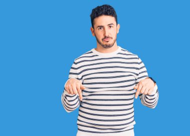 Gündelik kıyafetler giyen genç İspanyol adam üzgün ve üzgün görünüyor, parmaklarıyla yön gösteriyor, mutsuz ve depresif.. 