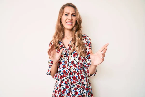 Young caucasian woman with blond hair wearing summer dress disgusted expression, displeased and fearful doing disgust face because aversion reaction. with hands raised