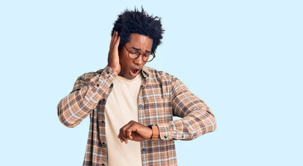 アフロの髪を持つハンサムなアフリカ系アメリカ人男性カジュアルな服や眼鏡を身に着けている時計の時間を心配し 遅くなるのを恐れて — ストック写真
