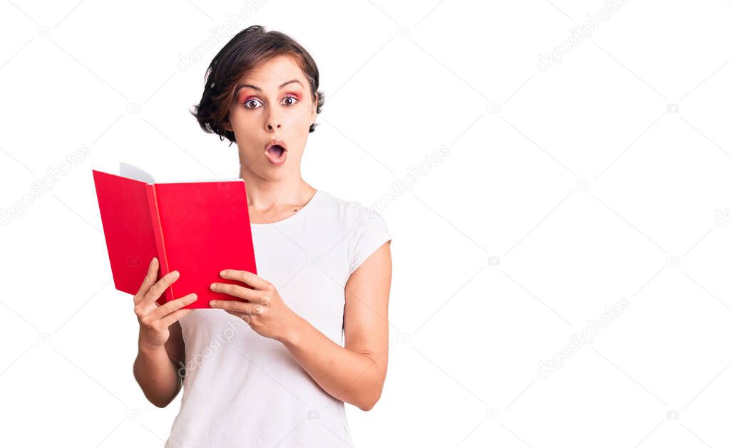 Beautiful young woman with short hair reading a book scared and amazed with open mouth for surprise, disbelief face 