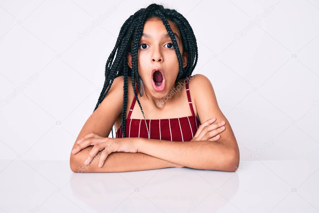 Young african american girl child with braids wearing casual clothes sitting on the table afraid and shocked with surprise expression, fear and excited face. 
