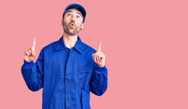 İspanyol ressam üniforması giyen genç adam şaşırmış ve şaşırmış bir şekilde yukarı bakıyor ve parmaklarıyla işaret ediyor ve kollarını kaldırıyor.. 