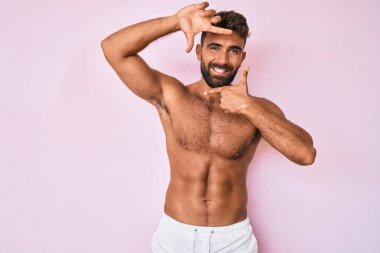 Genç İspanyol adam üstsüz gülümseyerek elleri ve parmakları gülen yüzlü bir çerçeve yapıyor. yaratıcılık ve fotoğrafçılık kavramı. 