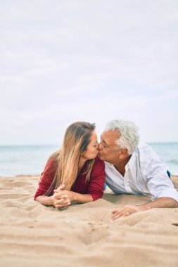 Orta yaşlı aşık bir çift kumsalda uzanmış birlikte mutlu ve mutlu öpüşüyorlar.