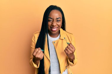 Genç Afro-Amerikalı kadın, gündelik ceket giyiyor. Çok mutlu ve heyecanlı. Kazanan jestler yapıyor, kolları havada, gülümsüyor ve başarı için bağırıyor. kutlama konsepti. 