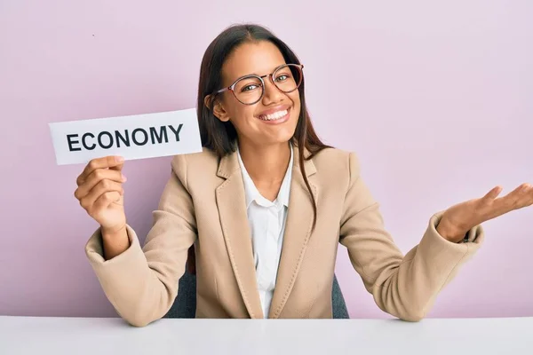 幸せな笑顔で達成を祝う経済のメッセージ用紙を保持し 手を上げて勝者の式を持つ美しいヒスパニックビジネス女性 — ストック写真