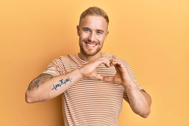 Gündelik çizgili tişört giyen beyaz bir genç aşık gülümsüyor elleriyle kalp sembolü yapıyor. romantik kavram. 