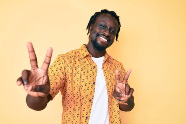 Saçları örgülü, gülümseyerek kameraya bakıp zafer işareti yapan Afro-Amerikalı genç bir adam. İki numara.. 