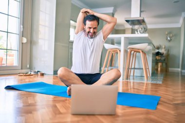 Orta yaşlı, sakallı ve esnek bir adam evde egzersiz yapıyor bilgisayardaki spor videolarına bakıyor.