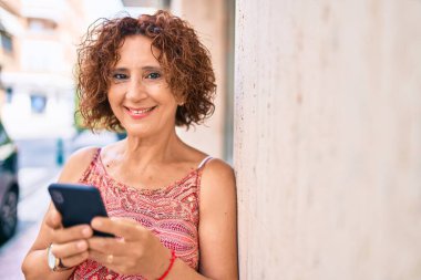 Şehir sokağında duvara dayanan akıllı telefon kullanan orta yaşlı kadın..