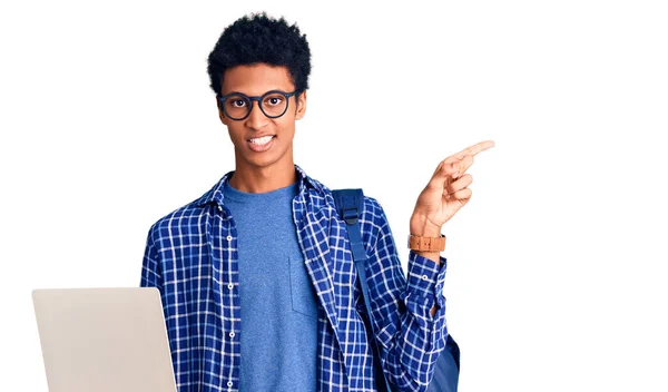若いですアフリカ系アメリカ人男性保持学生バックパック使用してラップトップ笑顔幸せなポインティングとともに手と指で側面 — ストック写真