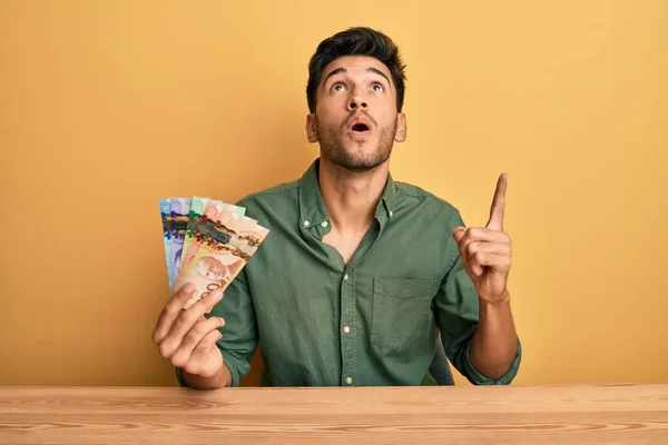 Joven Hombre Guapo Sosteniendo Dólares Canadienses Asombrado Sorprendido Mirando Hacia —  Fotos de Stock