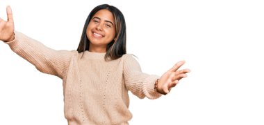 Kışlık yün kazak giyen genç Latin kız kucaklanmak için kollarını açmış kameraya bakıyor. Mutluluğu kucaklayan neşeli bir ifade.. 