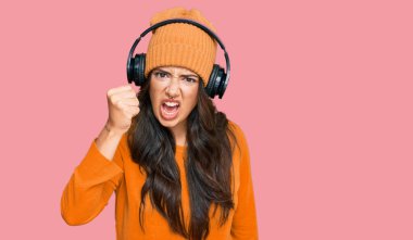 Güzel, esmer, genç bir kadın. Kulaklık takıp müzik dinliyor. Öfkeyle bağırırken kızgın ve kızgın yumruk kaldırıyor. öfke ve agresif konsept. 