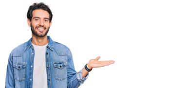 Gündelik kıyafetler giyen genç İspanyol adam neşeli bir şekilde gülümsüyor ve avuç içi kameraya bakıyor.. 