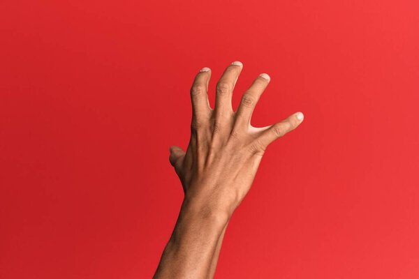 Hand of hispanic man over red isolated background grasping aggressive and scary with fingers, violence and frustration 