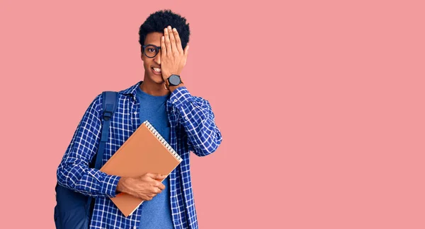 Joven Hombre Afroamericano Con Mochila Estudiantil Sosteniendo Libro Cubriendo Ojo —  Fotos de Stock