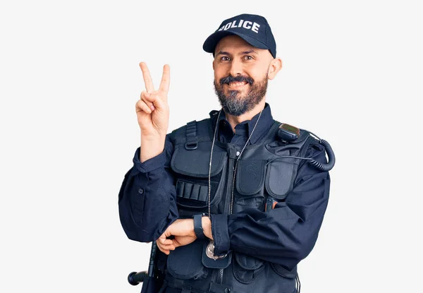 カメラでは幸せそうな顔をしながら笑顔で警察制服を着た若いハンサムな男が指で勝利サインをしています — ストック写真