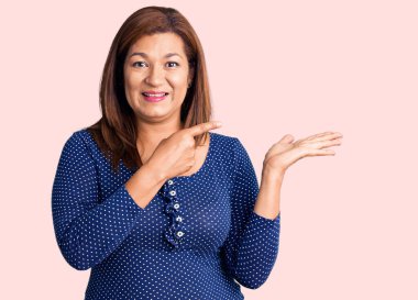 Orta yaşlı, güzel, günlük kıyafetler giyen, gülümseyen, mutlu, eli ve parmağı yana doğru olan bir kadın.