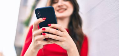 Genç beyaz kadın şehirde akıllı telefon kullanarak mutlu bir şekilde gülümsüyor..