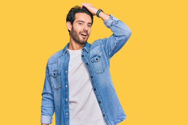 Gündelik kıyafetler giyen genç İspanyol adam gülümseyerek saçlarına dokunarak el hareketleriyle çekici ve modaya uygun bir poz veriyor. 