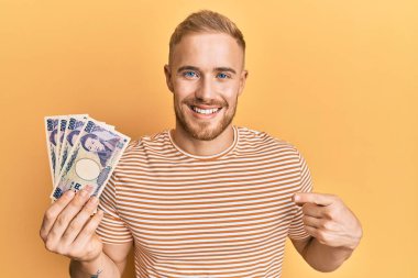 Elinde Japon Yen banknotları tutan genç beyaz adam mutlu bir şekilde elini ve parmağını gösterdi. 
