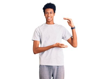 Genç Afrikalı Amerikalı sıradan kıyafetler giyen, elleri büyük ve büyük boy işareti gösteren, ölçü sembolü olan bir adam. Kameraya bakıp gülümsüyor. ölçüm kavramı. 