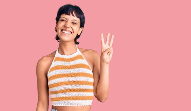 Kısa saçlı, esmer, günlük kıyafetler giyen, üç numaralı parmaklarıyla işaret eden, kendinden emin ve mutlu bir kadın.. 