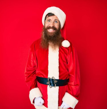 Uzun sakallı, yakışıklı, Noel Baba kostümü giyen yakışıklı genç adam. Pozitif ve mutlu görünüyor. Kendine güvenen bir gülümsemeyle dişlerini gösteriyor. 